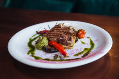 Sebzeli, sulu, iştah açıcı bir biftek, ızgarada pişirilmiş, yeşil soslu beyaz bir tabakta yatıyor..