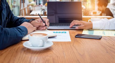 Ortağıyla birlikte projeyi sunmak için dizüstü bilgisayar kullanan işadamı not yazıyor