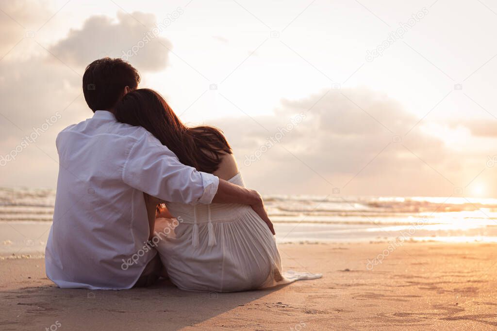 Couple in love watching sunset together on beach travel summer holidays. Romantic couple on the beach