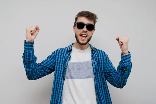 Gri arka planda izole edilmiş, kopyalama alanı olan yakışıklı bir genç. Heyecanlı sıradan hipster, mutluluk ve pozitif ifade gösteriyor. Heyecanlı sakallı adam poz verme modası.