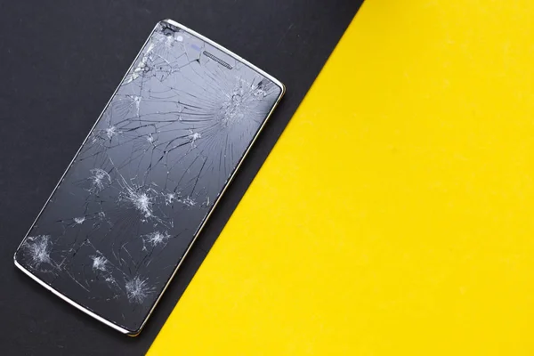 Un teléfono roto sobre fondo amarillo y negro. Dispositivo aplastado con pantalla rota que representa un accidente. Pantalla texturizada con daño. El cristal oscuro de la pantalla . — Foto de Stock