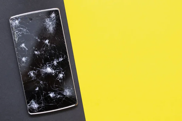 Un teléfono roto sobre fondo amarillo y negro. Dispositivo aplastado con pantalla rota que representa un accidente. Pantalla texturizada con daño. El cristal oscuro de la pantalla . — Foto de Stock