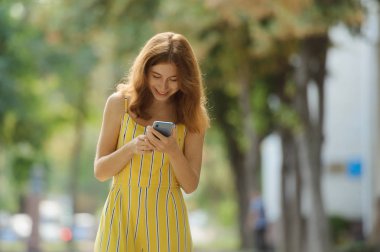 Genç kızıl saçlı kız öğrenci telefonunu izliyor ve gülümsüyor..