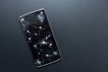 Siyah arka planda kırılmış bir telefon. Kırık ekranlı ezilmiş cihaz bir kazayı temsil ediyor. Hasarlı ekran. Kırık bir ekranın siyah camı..
