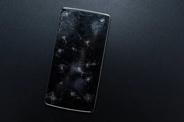 Un teléfono roto sobre fondo negro. Dispositivo aplastado con pantalla rota que representa un accidente. Pantalla texturizada con daño. Cristal oscuro de una pantalla, roto . — Foto de Stock