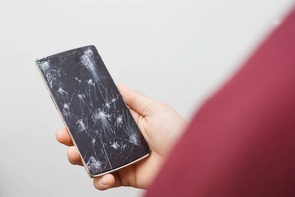 Un hombre sosteniendo un celular después de un accidente. Teléfono digital con pantalla rota . — Foto de Stock