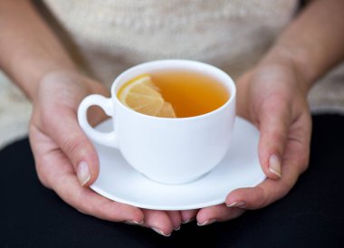 Bir bardak limonlu çay, iki elle kapatılmış.