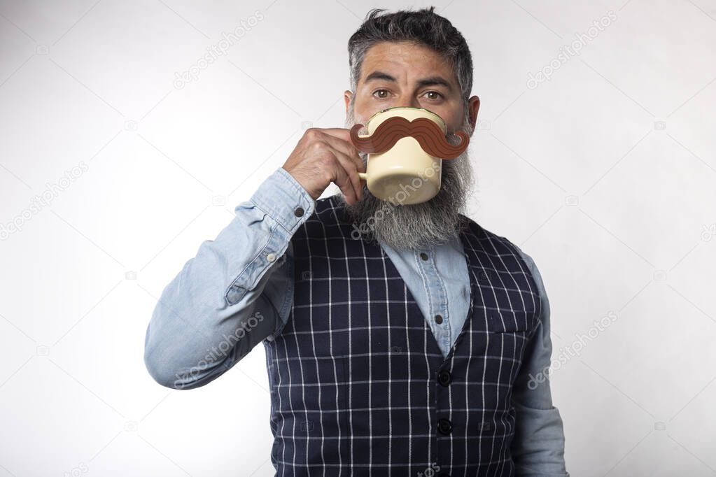 Portrait of bearded man drinking from a cup with a fake paper mustache on white background.