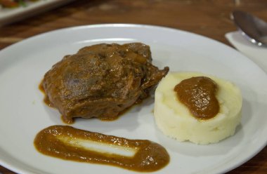 Ahşap zemin üzerinde patates püresiyle servis edilen soslu domuz rostosu.