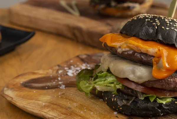 Delicious homemade burger of black bread with double burger of 200 grs. , lettuce, tomato, mimolete cheese, gruyre, semi-cured and taleggio on wooden board. Close-up with copy space.