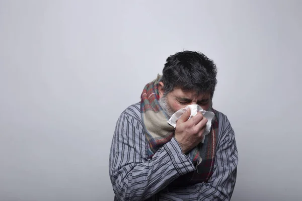 Homem adulto soprando o nariz de um resfriado em um fundo cinza. febre aftosa — Fotografia de Stock
