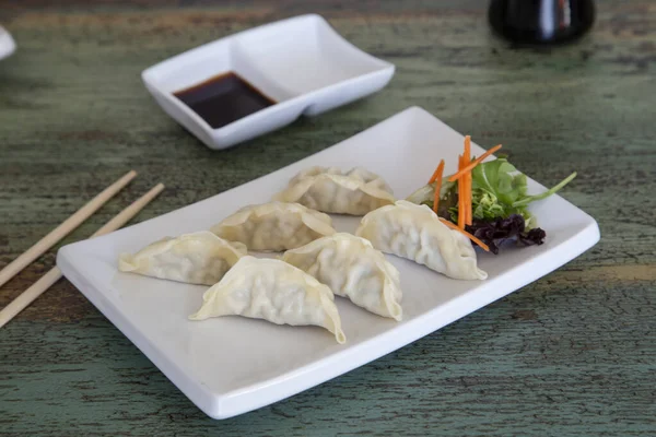 Petits pains coréens Mandu cuits à la vapeur avec viande de poulet et légumes sur une assiette blanche sur fond de bois . — Photo