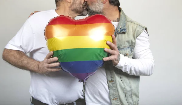 Однополые пары целуются, держа шарик цвета ЛГБТ-радуги на белом фоне. День святого Валентина — стоковое фото