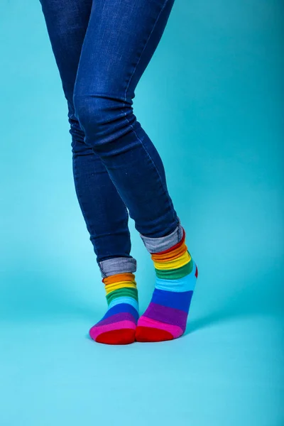 Γυναίκα με μπλε τζιν σταυρώνει τα πόδια της με χρωματιστές κάλτσες lgtbi σε μπλε φόντο. Μεμονωμένη εικόνα. — Φωτογραφία Αρχείου