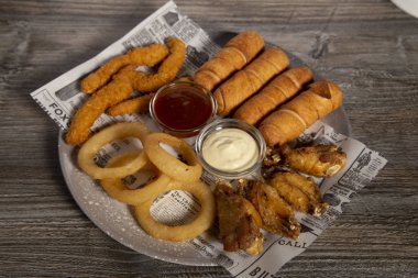 Karışık tavuk şeritleri, soğan halkaları, tavuk kanatları ve ahşap arka planda soslu tequeñolar. Üst görünüm