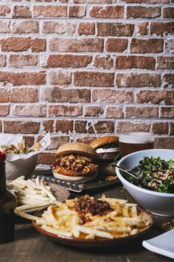 Çeşitli tabaklar, hamburgerler, patates kızartması ve salata, içecekler ve ahşap masada sos. Restoran menüsü. Dikey resim