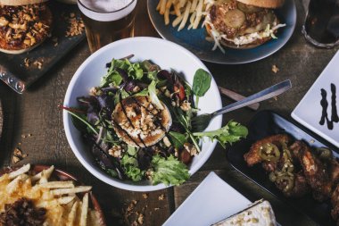 Tabakların, hamburgerlerin, patates kızartmalarının ve salatanın olduğu masa manzarası. Restoran menüsü.