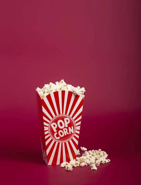 Kırmızı arka planda çizgili kovada patlamış mısır. Karton kutudan çıkan sıcak mısır, kopyalama alanı. Fast food ve film atıştırmalığı..