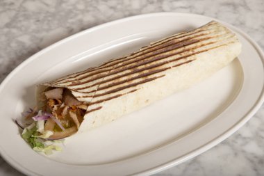 Sert ekmeğin içinde beyaz mermer masada servis edilen Durum kebabı..