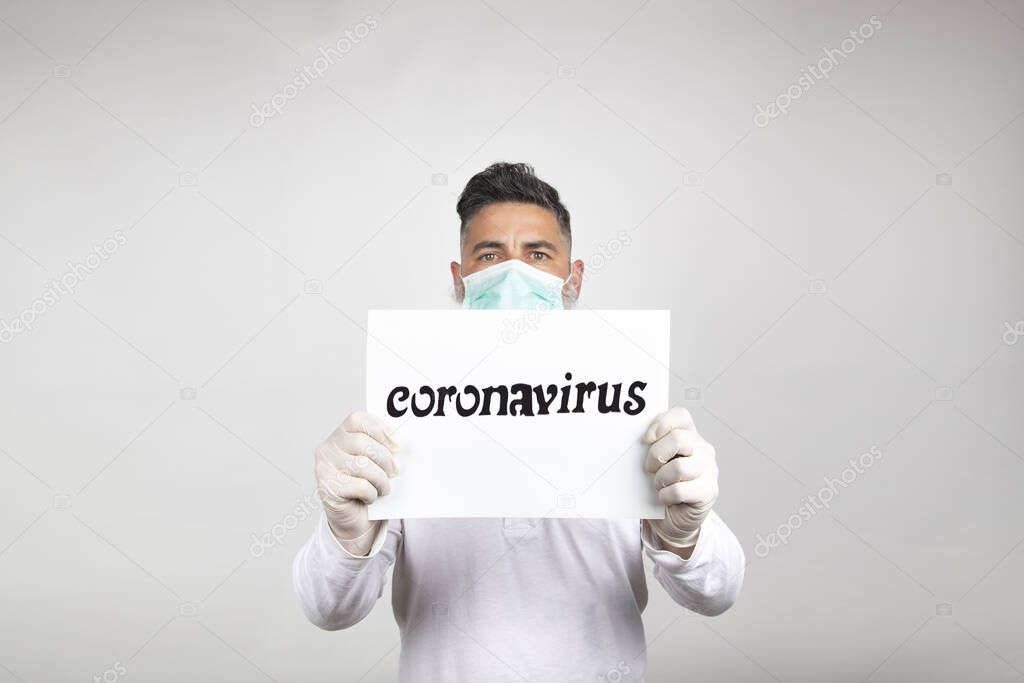 Portrait of man in surgical mask holding a white sign with the word coronavirus on white background.