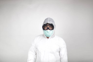 Koronavirüse karşı önleyici tedbir olarak cerrahi maske takan ve koruyucu giysili bir adamın portresi. Beyaz arkaplanda resim.