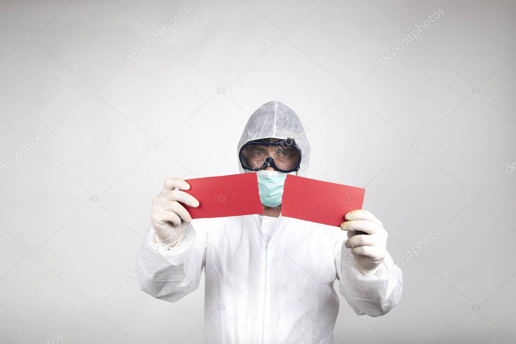 Man in surgical mask with white protective suit and a red halved poster isolated in studio on white background. Prevention against coronavirus.