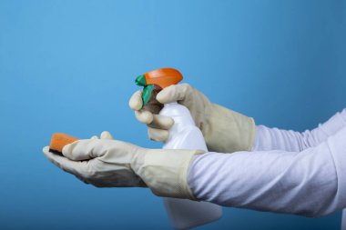 Süngerli sarı bir eldiven, mavi arka planda temizleme sıvısı olan bir şişenin yanında. Coronavirüs dezenfeksiyonu