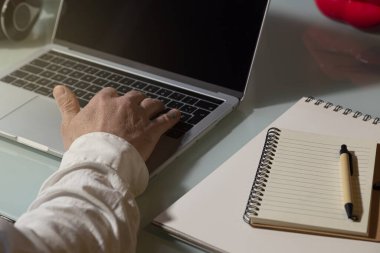 Evden çalışmak için bilgisayarı kullanan bir adamın eli. Not defteri, kalem masaya. Telework konsepti