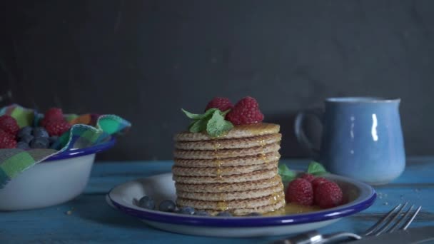 Stapelweise Holländische Pfannkuchen Mit Honig Und Beeren Auf Blauem Holztisch — Stockvideo