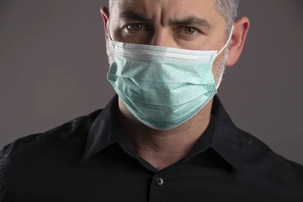 Portrait of a man with medical facial mask who is concerned about preventing pandemic coronavirus on a gray background.