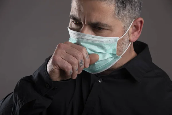 Close-up of man with surgical mask coughing on gray background, healthcare concept. Coronavirus