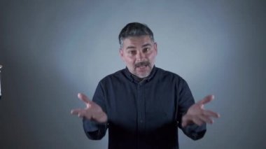 Beyaz arka planda mavi kot gömlekli bir adam İspanyolca işaret diliyle selam veriyor. NasıIsın? Ben iyiyim. Öğrenme kavramı.