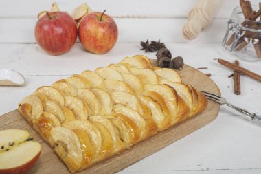 Elmalı turtaya yakın çekim ve tahta kesme tahtasının üzerinde brioche hamur var. Beyaz tahta masada hayat devam ediyor..