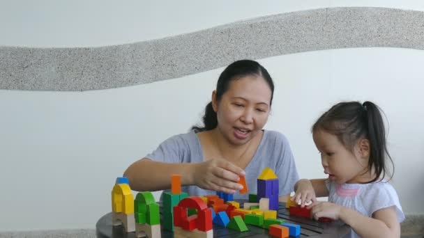 Девочка и мама играют с деревянными блоками на столе — стоковое видео