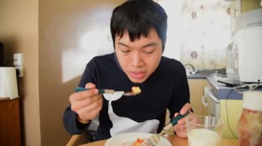 Genç Asyalı adam yeme kahvaltı mutfak masasının