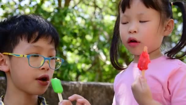 Malé asijské sourozenci spolu jíst zmrzlinu v parku 