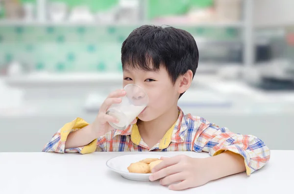 Niño comiendo galletas con leche en la cocina —  Fotos de Stock