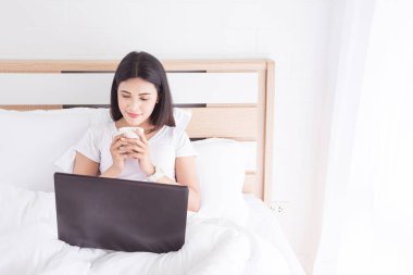 Yatağın üstüne oturup, kahve içme ve tablet bilgisayarı kullanan kadın