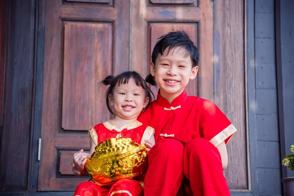 Feliz asiático irmãos no chinês tradicional traje segurando ouro dinheiro banco — Fotografia de Stock