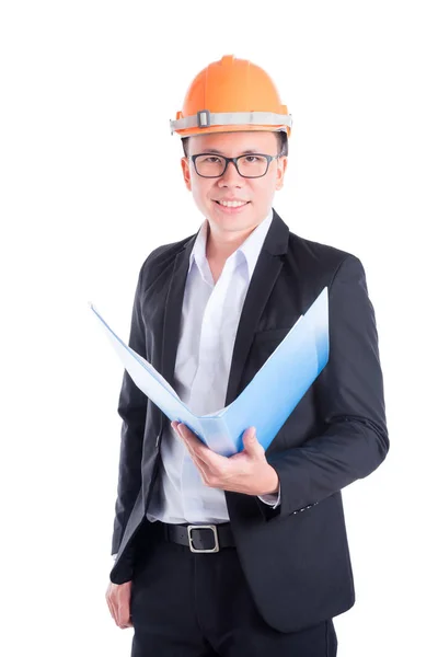 Młody inżynier człowiek ubrany w czarny garnitur uśmiechający się nad biały i pomarańczowy kask — Zdjęcie stockowe
