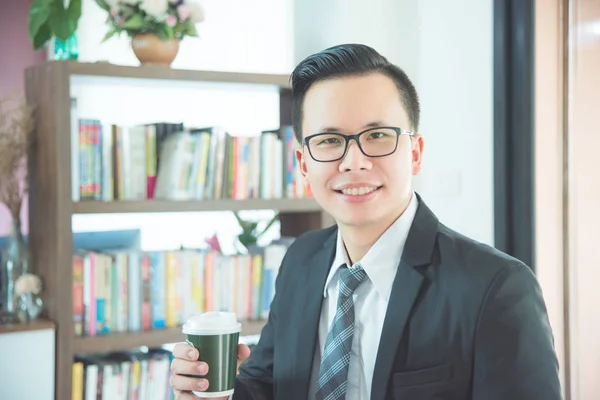 Homme d'affaires tenant tasse de café et souriant dans le bureau — Photo