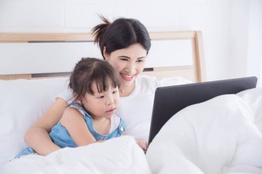 Anne ve kızı yatağa dizüstü bilgisayar kullanan