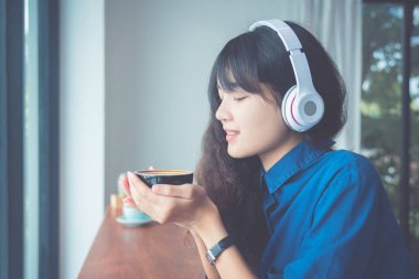 Kahve fincanı ve müzik dinleme sırasında gülümsüyor tutan genç kadın