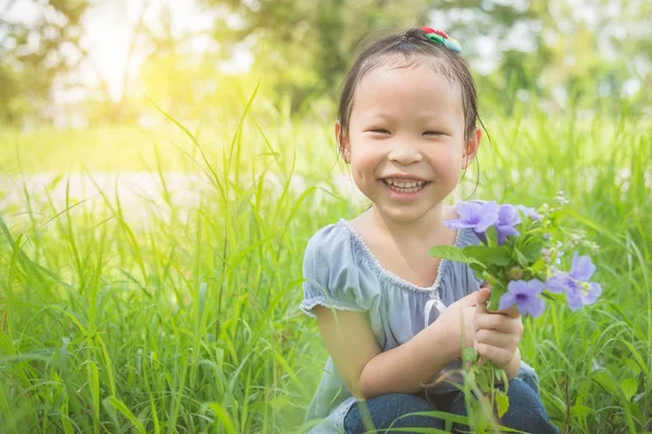 Маленька дівчинка посміхається, тримаючи квітку в саду — стокове фото
