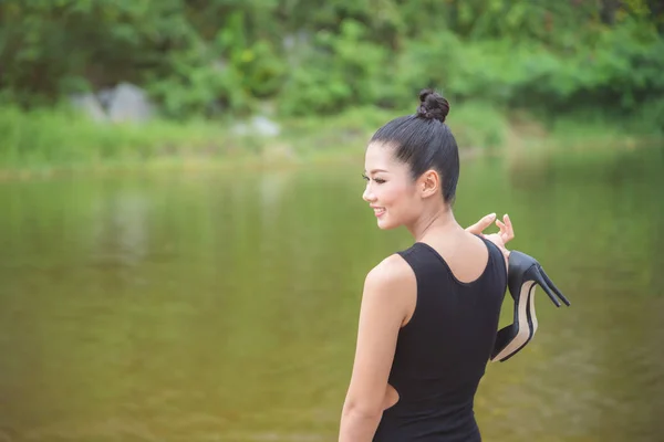 Menina em vestido preto segurando sapatos de salto alto e sorrisos — Fotografia de Stock