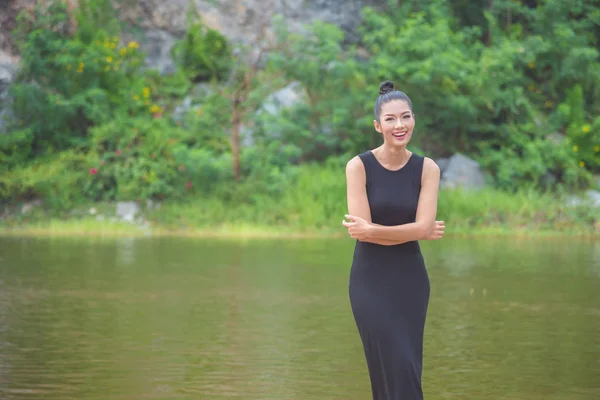 Menina em vestido preto sorrindo perto do rio — Fotografia de Stock