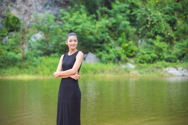 Menina em vestido preto sorrindo perto do rio — Fotografia de Stock