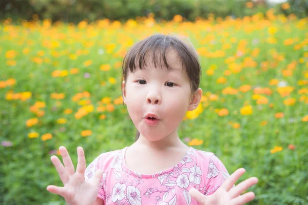 Ragazza con la faccia sorpresa in piedi nel parco dei fiori — Foto Stock