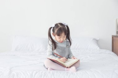 kız yatakta oturuyor ve alfabe defter üzerinde yazma