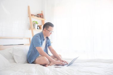 Yatağın üstüne oturan ve evde dizüstü bilgisayar kullanarak bir adam
